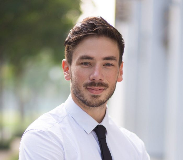 Ambitious businessman standing in street and looking at camera. Serious young manager crossing arms on chest and enjoying success. Confidence concept